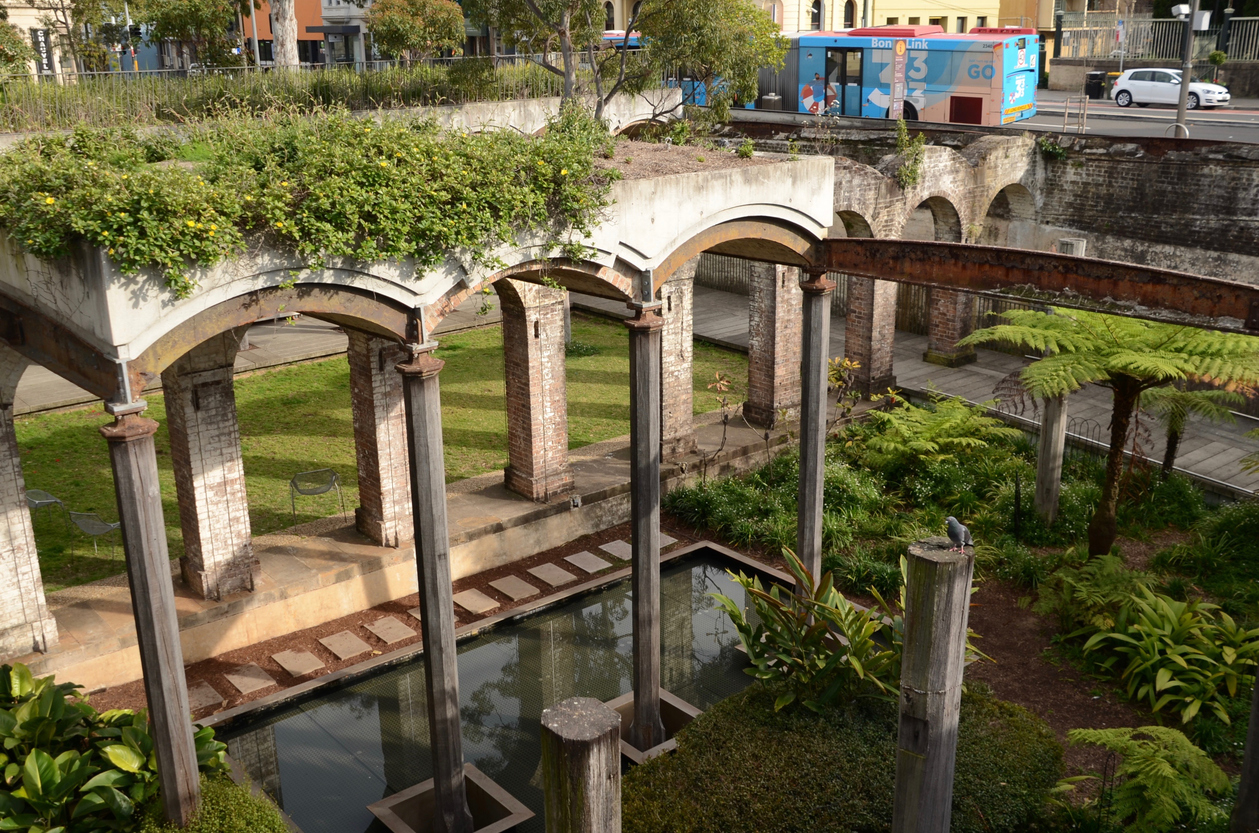 Paddington Reservoir Gardens with old stone arches reflected in pool. Oxford Street in the background with bus